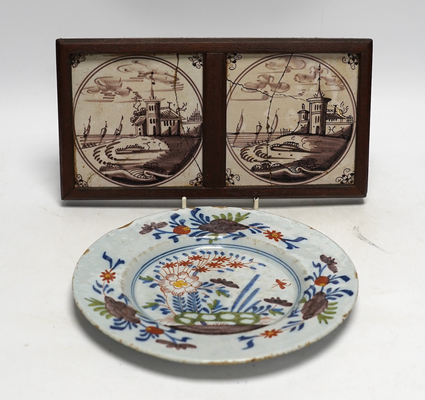 An 18th century Delft polychrome plate, 23cm diameter, and two framed tiles. Condition - tiles poor, plate with usual chipping to edges